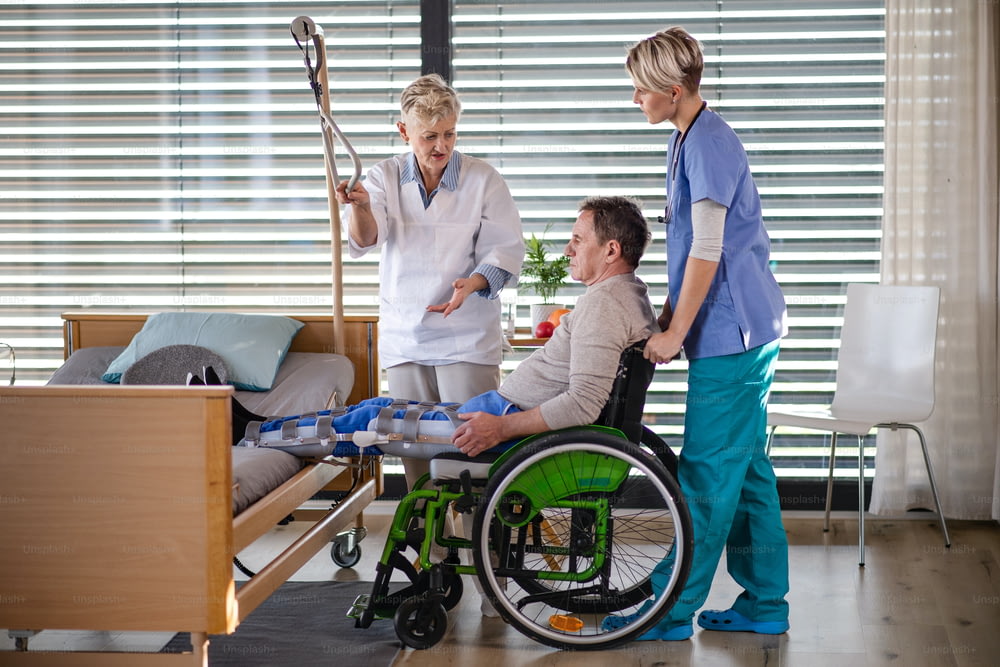 Mulheres profissionais de saúde e paciente idosa em cadeira de rodas no hospital, falando.