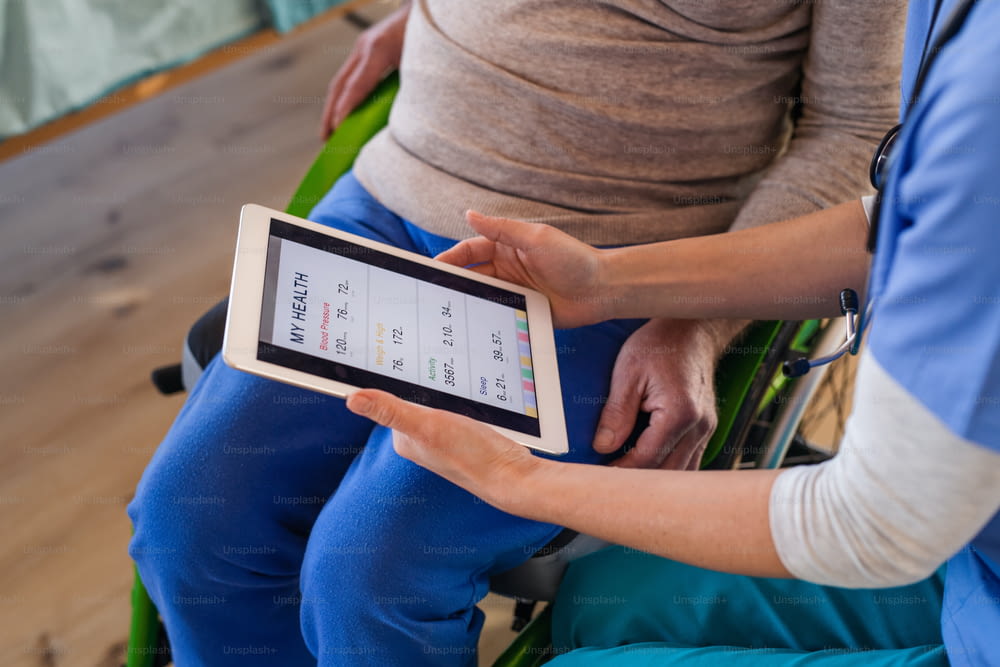 Un abdomen de médecin avec tablette et un patient en fauteuil roulant à l’hôpital, en train de parler.