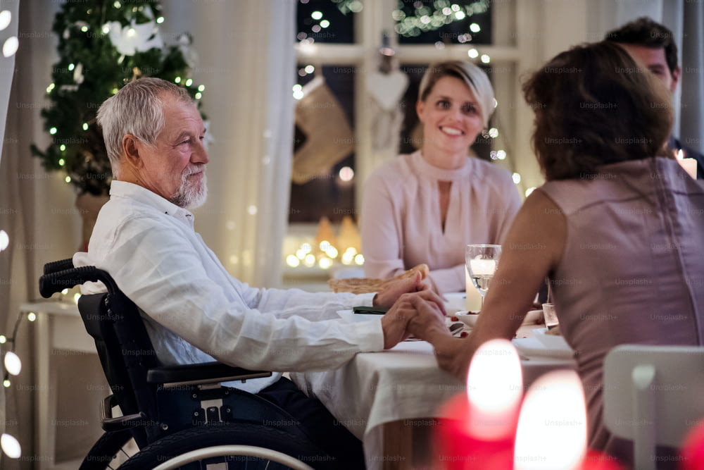 Glücklicher älterer Mann im Rollstuhl mit Familie drinnen, die gemeinsam Weihnachten feiert.