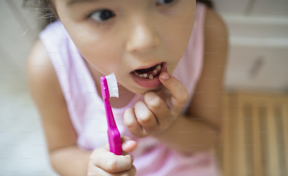 Vue de dessus portrait d’une petite fille inquiète avec une brosse à dents à l’intérieur, perdant une dent de lait.