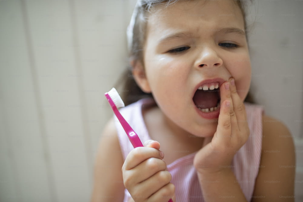 Portrait de face d’une petite fille inquiète avec une brosse à dents à l’intérieur, perdant une dent de lait.