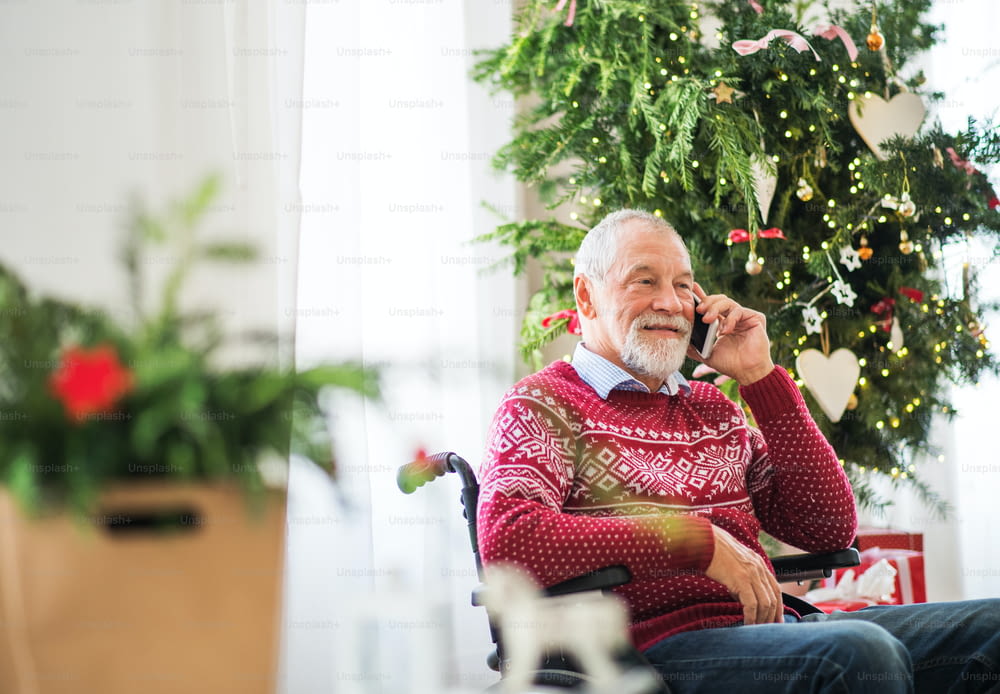 A senior man in wheelchair with a mobile phone at home at Christmas time, making a phone call.