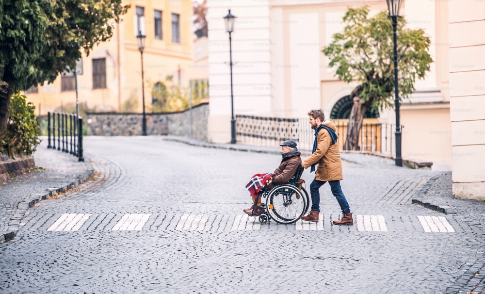 Père en fauteuil roulant et jeune fils en promenade. Un soignant aidant un homme âgé handicapé.
