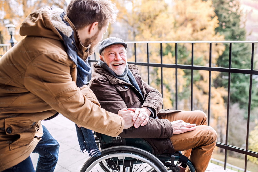 Vater im Rollstuhl und kleiner Sohn auf einem Spaziergang. Ein Betreuer, der einem behinderten älteren Mann hilft.