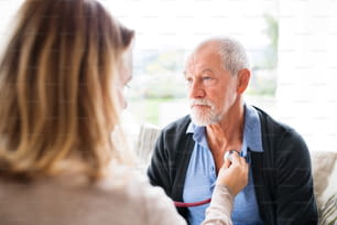 Visitante de saúde e um homem idoso durante a visita domiciliar. Uma enfermeira ou um médico examinando um homem.