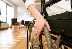 Giovane donna disabile irriconoscibile in sedia a rotelle a casa nel suo salotto. Primo piano del suo braccio posato sulla ruota.