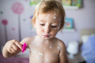 Little two year old girl at home sick with chickenpox, white antiseptic cream applied to the rash. Playing with bubble blower, blowing bubbles.