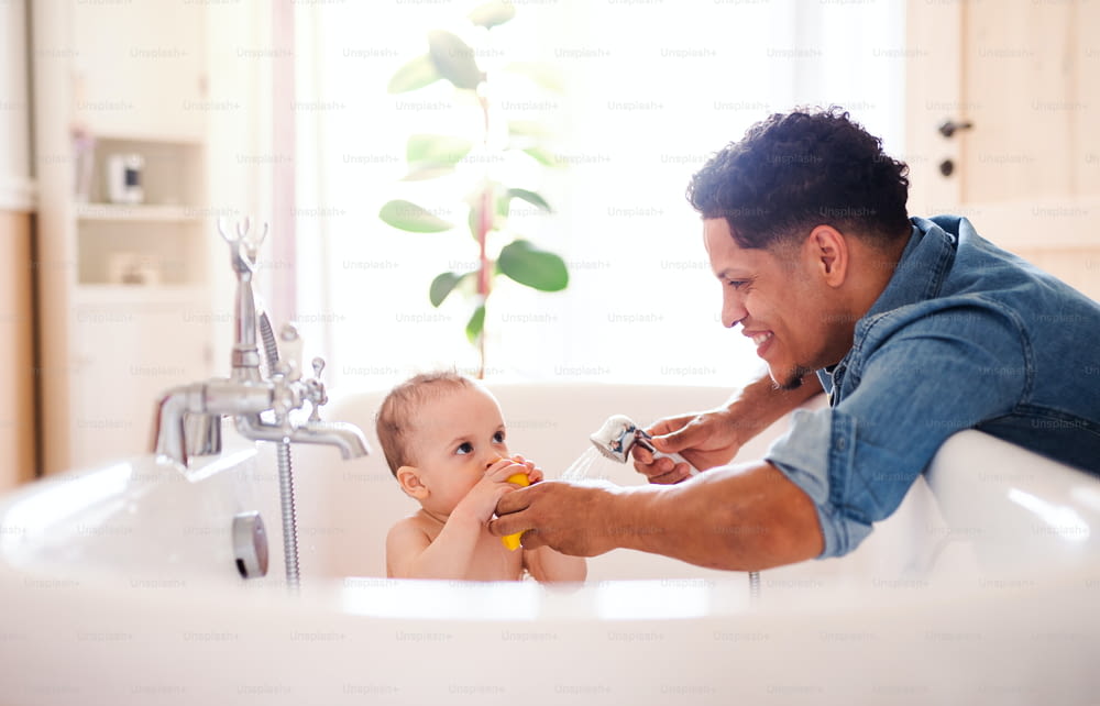 ヒスパニック系の父親が自宅の屋内のバスルームで小さな幼児の息子を洗う。
