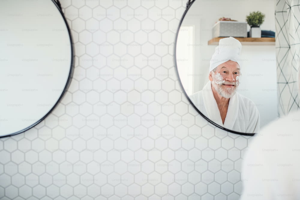 A senior man doing morning routine in bathroom indoors at home, looking in mirror. Copy space.