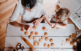 A top view of senior grandmother with small toddler boy making and decorating cakes at home.