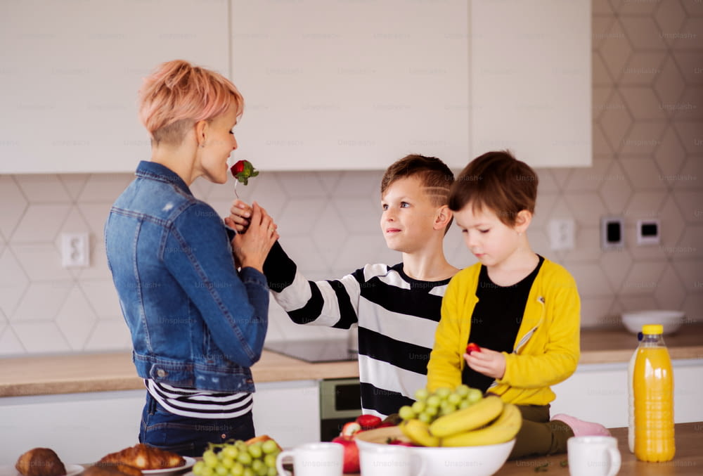 A young woman with two happy children eating fruit in a kitchen.