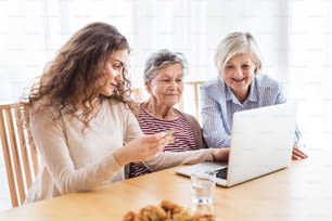 Una ragazza adolescente, sua madre e sua nonna con il computer portatile a casa. Concetto di famiglia e generazioni.
