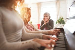 Ein nicht wiederzuerkennendes Teenager-Mädchen mit Mutter und Großmutter, die zu Hause Klavier spielen. Familien- und Generationenkonzept.