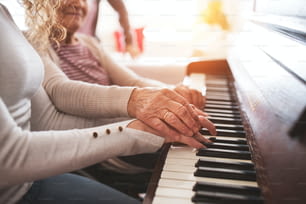 Ein nicht wiederzuerkennendes Teenager-Mädchen mit Großmutter, die zu Hause Klavier spielt. Familien- und Generationenkonzept.