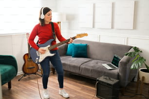 Giovane donna appassionata che canta una canzone mentre suona la chitarra elettrica collegata a un amplificatore