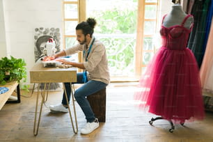 Jovem criativo e costureira costurando um novo vestido elegante para um cliente no estúdio