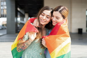 Casal gay feliz abraçando com uma bandeira do arco-íris em torno de seus ombros e celebrando o orgulho gay