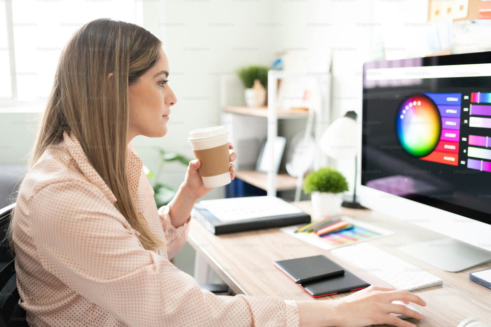 Mujer bastante creativa y diseñadora bebiendo una taza de café mientras hace un trabajo en su oficina