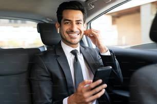 Sorridente bell'uomo d'affari che ascolta la musica attraverso gli auricolari wireless mentre viaggia in auto