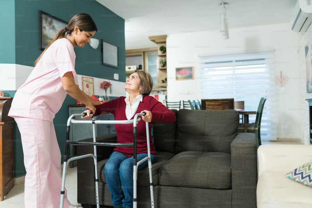 Confident nurse helping senior disabled woman to walk with mobility walker at home