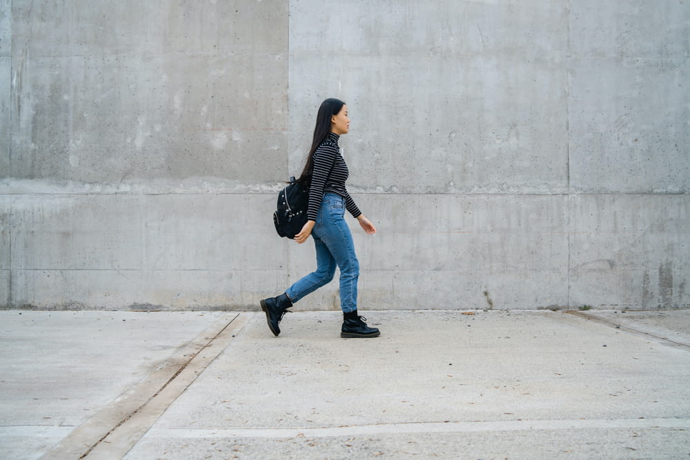 Retrato de una joven y hermosa mujer asiática caminando contra una pared de hormigón gris.