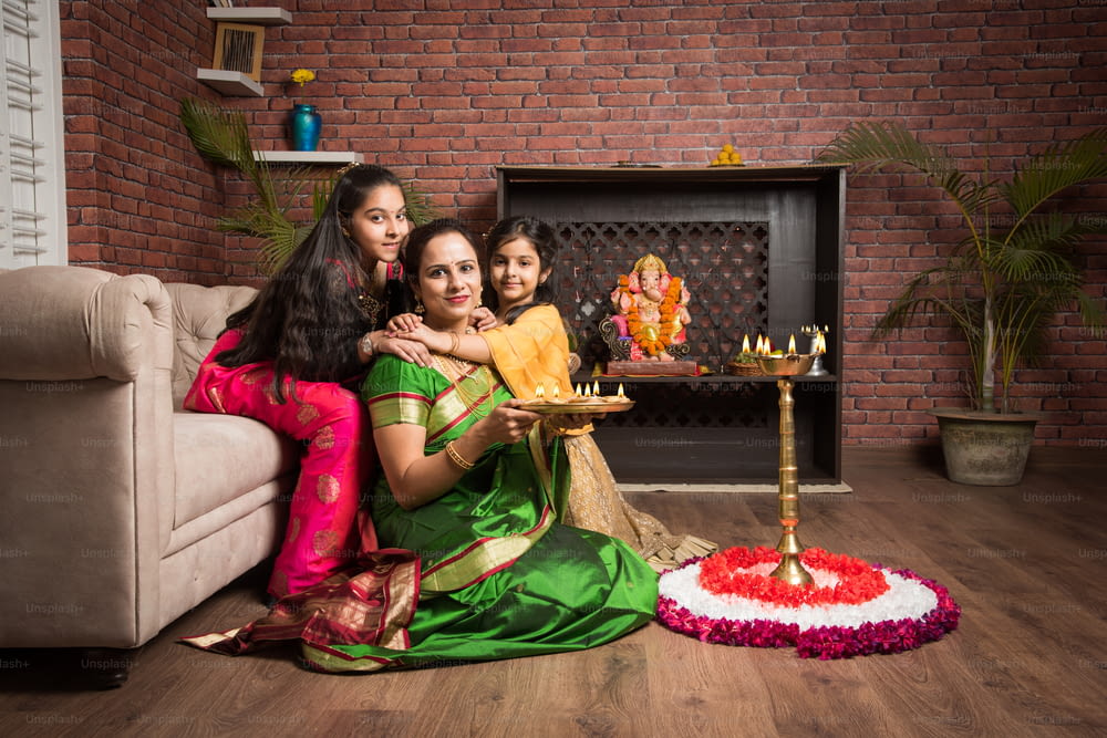 Mutter und Tochter machen Blumen-Rangoli und Mädchen zünden Diya oder Samai an