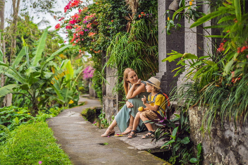 バリ島の母と息子の観光客は、ウブドの狭い居心地の良い通りを歩きます。バリ島は人気のある観光地です。バリへの旅行のコンセプト。子供との旅行のコンセプト。