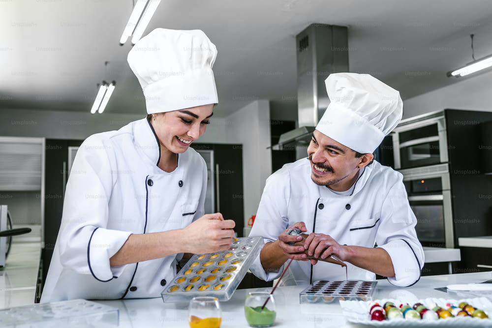 young latin couple woman and man chocolatier in chef uniform and hat preparing mexican chocolates bonbon candies at kitchen in Mexico Latin America