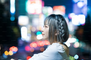 Giovane donna che posa nel paesaggio urbano luminoso di Tokyo di notte