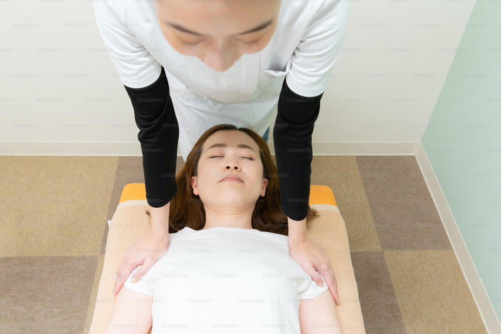 Asian female practitioner massaging shoulders and neck of female patient
