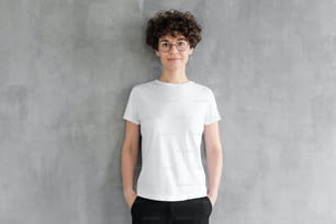 Giovane donna attraente che posa in t-shirt di cotone bianco bianco, in piedi contro il muro grigio strutturato