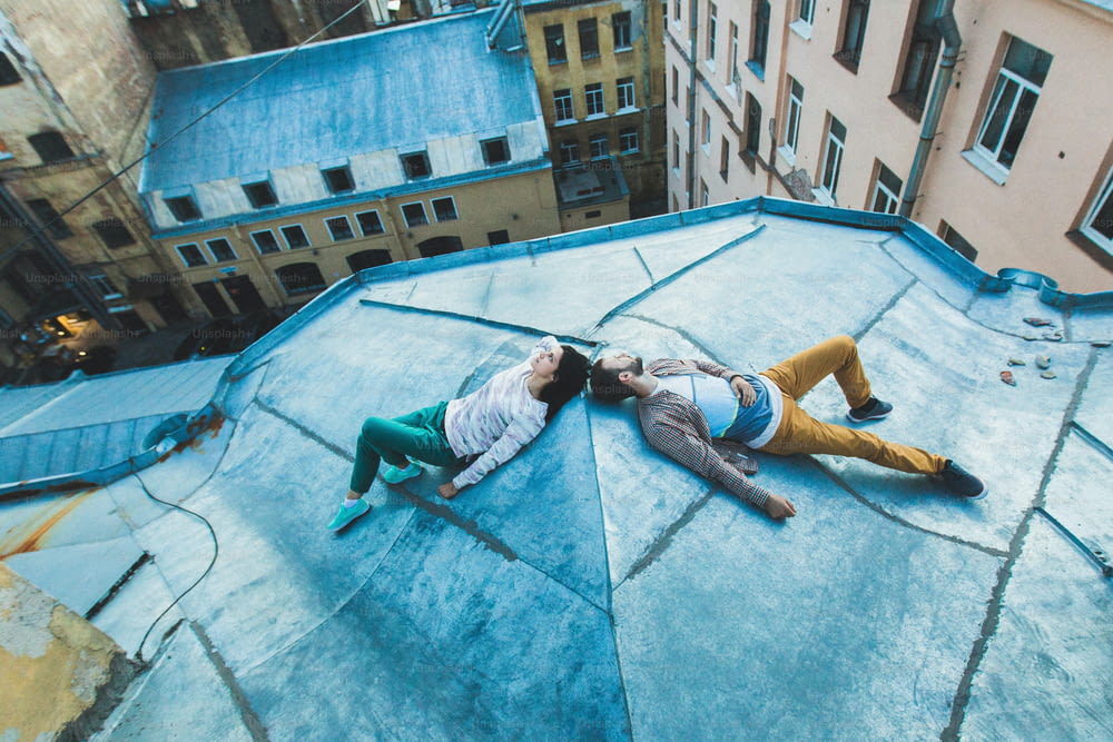 屋根の上に横たわってキスをする若いヒップスター夫婦。上からの街の美しい景色。カジュアルスタイル