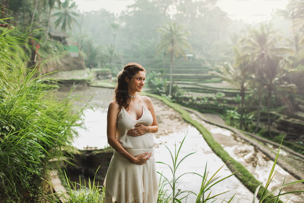Giovane donna incinta in vestito bianco con vista delle terrazze di riso di Bali alla luce del sole del mattino. Armonia con la natura. Concetto di gravidanza.