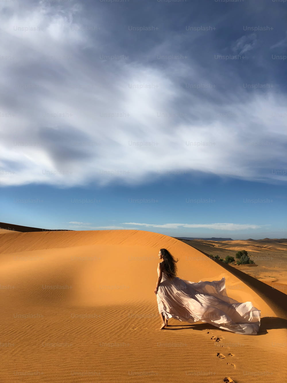 Femme en robe de mariée en soie étonnante avec vue fantastique sur les dunes de sable du désert du Sahara à la lumière du coucher du soleil. Paysage du Maroc, Afrique.