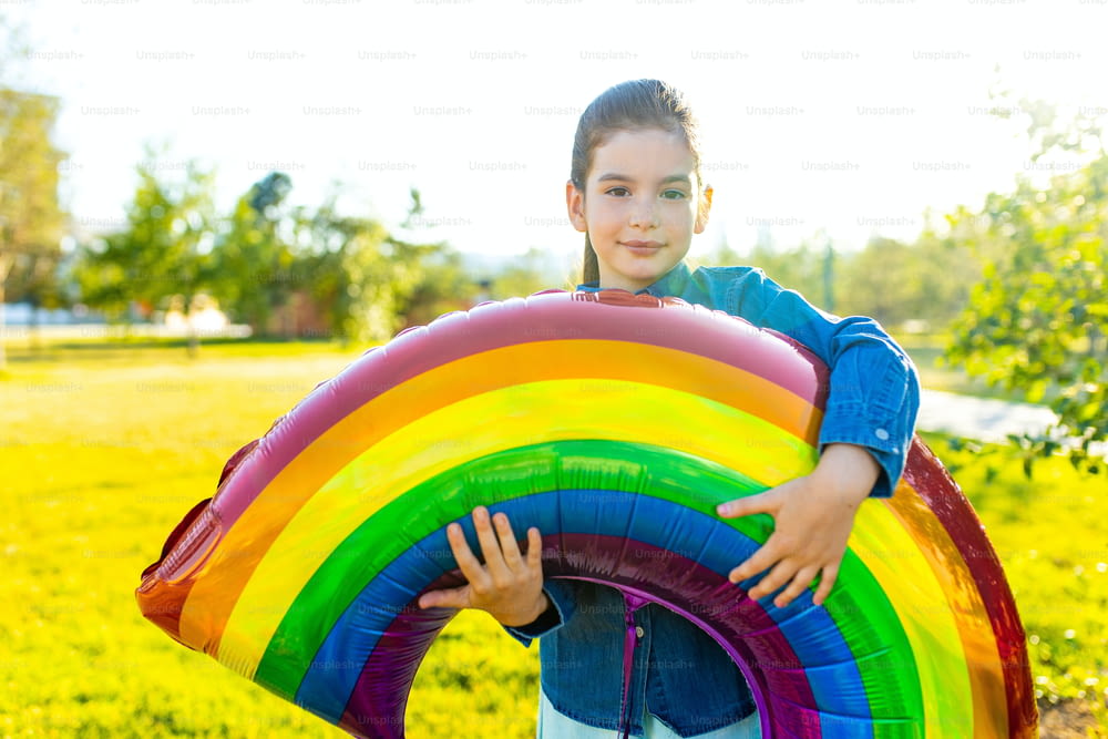beautiful latin hispanic seven years old girl with big rainbow balloon outdoors in summer park.