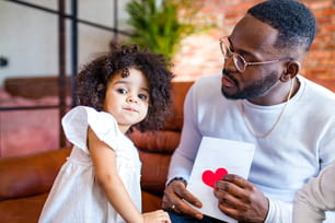 afro american baby giving to dad a Valentine's Day picture in living room .