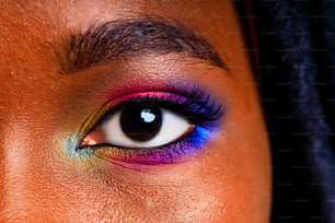 Fêmea com maquiagem arco-íris e cílios longos em baclground estúdio azul.