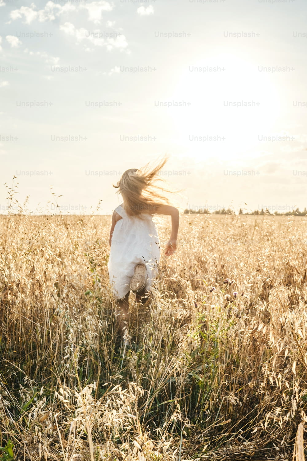 Little girl running on meadow in the distance. Sunset light, copy space. Back view.