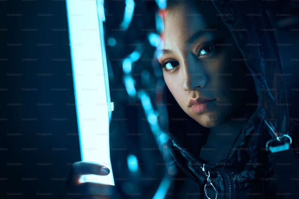 Futuristic portrait of asian teenager in neon light. She is seriour, daring, cyberpunk fashionable girl