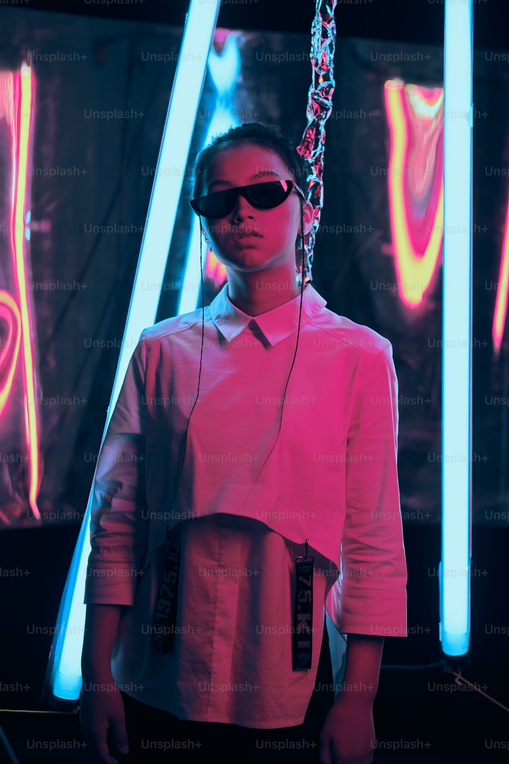 Portrait d’une jeune adolescente asiatique portant d’élégantes lunettes de soleil en forme de croissant, en néon rouge et bleu. Cyber, concept de portrait futuriste