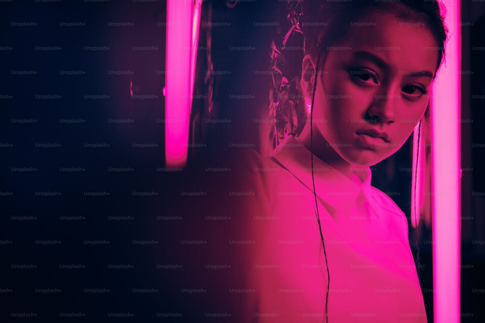 Retrato da jovem adolescente asiática com a mão em direção à câmera, em luz neon roxa. Conceito de retrato cibernético e futurista