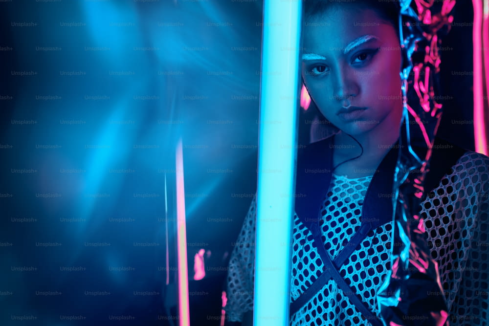 Retrato futurista de adolescente asiático em luz neon com espada como lâmpadas. Efeitos borrados de néon aplicados na frente. Ela é seriada, ousada, cyberpunk garota da moda, em roupas de rede, sobrancelhas brancas