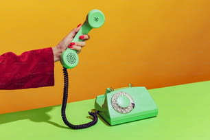 옛날 초록색 전화기를 들고 있는 여성의 화려한 밝은 이미지, 주황색 배경 위에 고립된 핸드셋을 들고 있다. 팝 아트의 개념, 빈티지 물건, 옛 것과 현대의 혼합