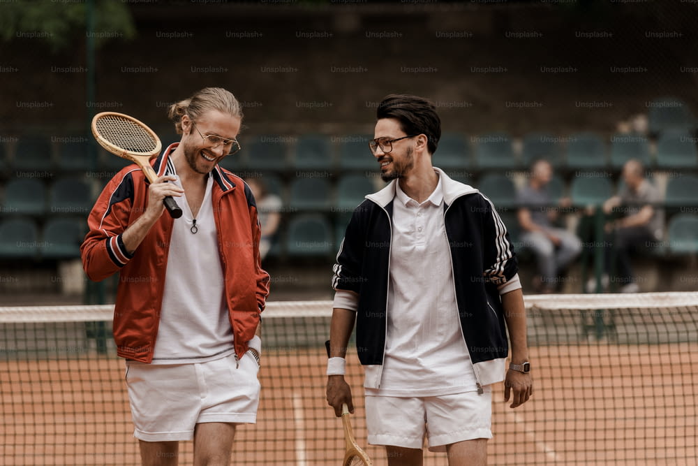 smiling retro styled tennis players walking with rackets at tennis court