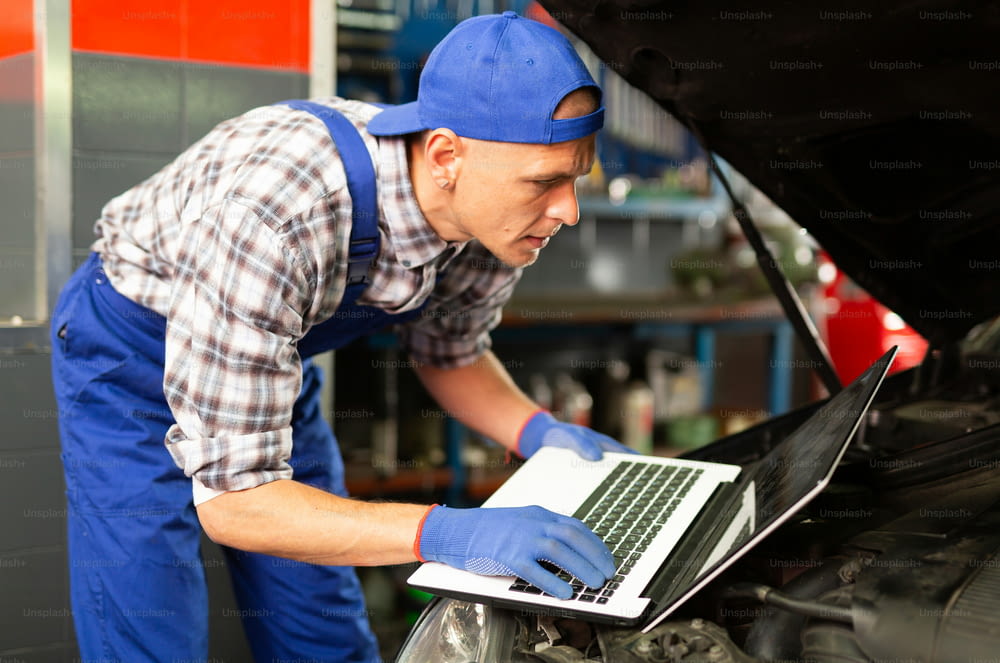 Mechanic with laptop near car engine in auto service