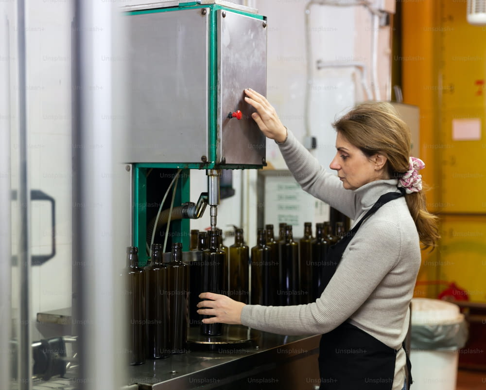 Mujer experta dedicada a la producción de aceite de oliva, controlando el proceso de embotellado del producto terminado en botellas de vidrio