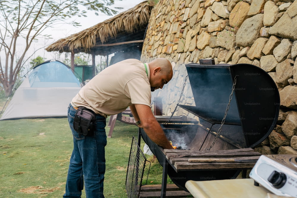 a man standing over a bbq grill in a field
