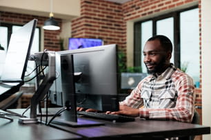 Selbstbewusster kreativer Büroangestellter, der am Computer im Büroarbeitsplatz sitzt, während er digitale Kunst entwickelt. Professioneller Grafikdesigner sitzt am Schreibtisch, während er an einem Projekt arbeitet.