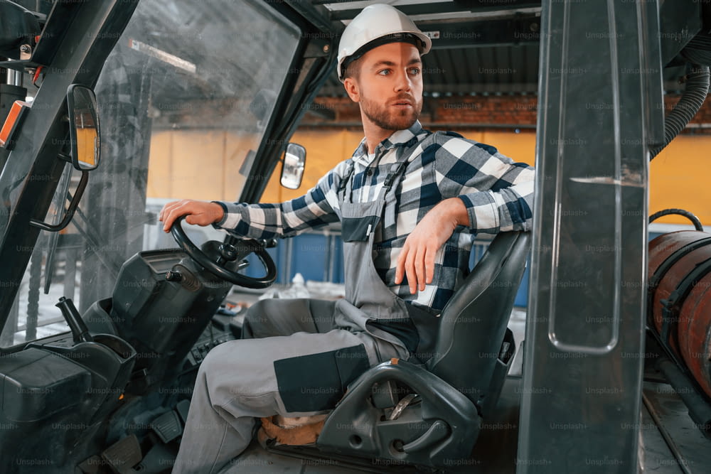 Driving the forklift. Factory male worker in uniform is indoors.