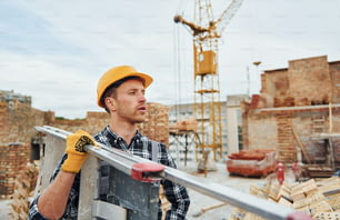 Escada nas mãos. Trabalhador da construção civil em uniforme e equipamentos de segurança tem trabalho na construção.